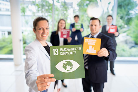 5 Personen halten Karten mit den UN-Zielen in der Hand. Im Vordergrund eine Karte mit dem Text Maßnahmen zum Klimaschutz