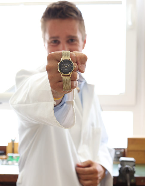 Ein junger Mann hält eine goldene Uhr in die Kamera.