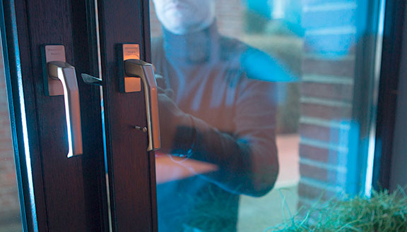 Ein dunkel gekleideter Einbrecher öffnet ein Fenster.