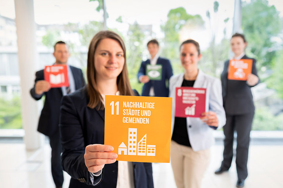 Mitarbeiter der NRW.BANK halten Karten mit Symbolen der Sustainable Development Goals hoch.
