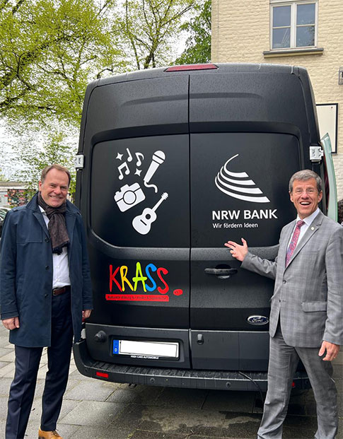 Stephan Keller, Oberbürgermeister der Stadt Düsseldorf, und Eckhard Forst, Vorstandsvorsitzender der NRW.BANK, stehen vor einem schwarzen Transporter mit dem Logos des Vereins Krass e. V. und der NRW.BANK.