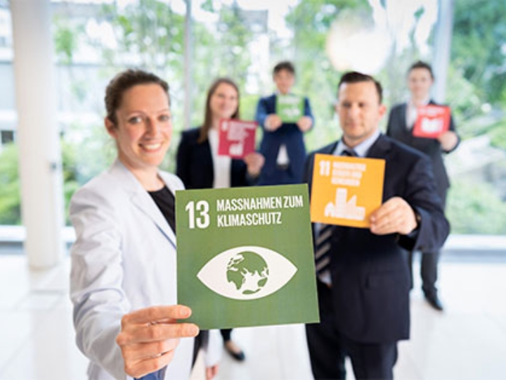 5 Personen halten Karten mit den UN-Zielen in der Hand. Im Vordergrund eine Karte mit dem Text Maßnahmen zum Klimaschutz