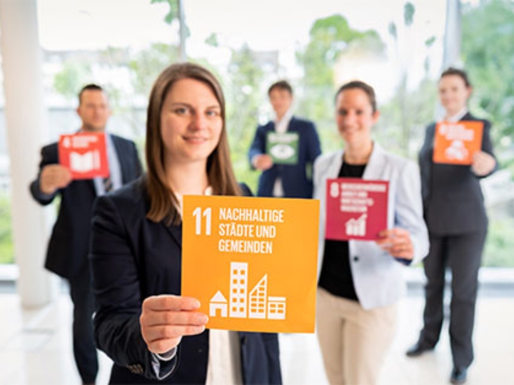 5 Personen halten Karten mit den UN-Zielen in der Hand. Im Vordergrund eine Karte mit dem Text Nachhaltige Städte und Gemeinden
