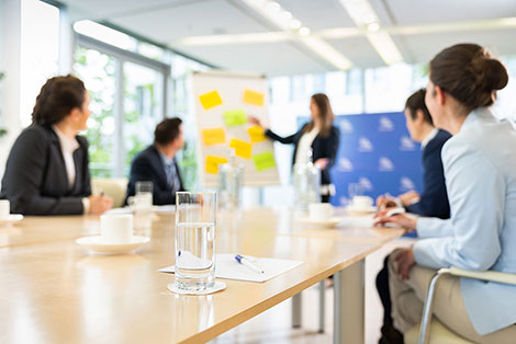 Seminarteilnehmer sitzen an einem Tisch, vor dem eine Frau an einem Flipchart etwas erklärt.