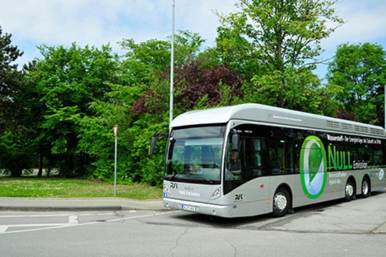 Ein moderner Linienbus, der mit Wasserstoff angetrieben wird, auf einer Straße vor einem Park