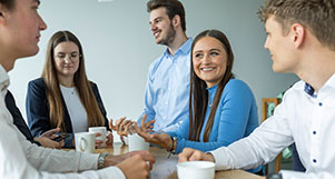 Eine Gruppe dual Studierender steht an einem Tisch und trinkt Kaffee