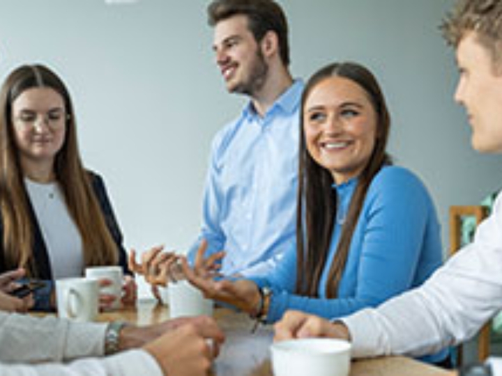 Eine Gruppe dual Studierender steht an einem Tisch und trinkt Kaffee