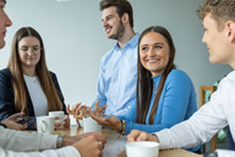 Eine Gruppe dual Studierender steht an einem Tisch und trinkt Kaffee
