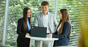 Drei junge Mitarbeiter und Mitarbeiterinnen der NRW.BANK stehen um einen Laptop und lachen