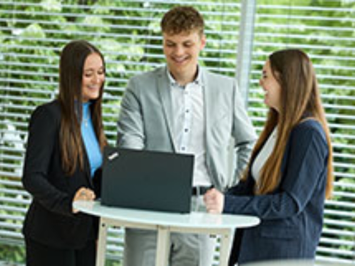 Drei junge Mitarbeiter und Mitarbeiterinnen der NRW.BANK stehen um einen Laptop und lachen