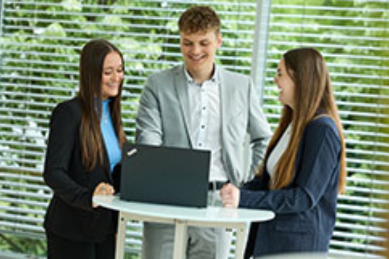 Drei junge Mitarbeiter und Mitarbeiterinnen der NRW.BANK stehen um einen Laptop und lachen