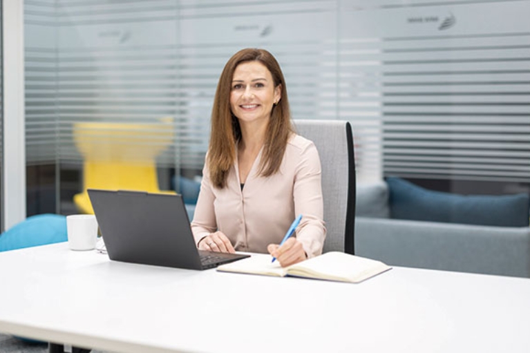 Judith hat ihren Laptop in einem hellen Büro vor sich aufgeklappt und macht sich Notizen.