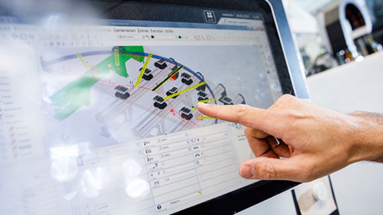 Ein Finger zeigt auf einen Monitor, auf dem eine technische Zeichnung zu sehen ist.