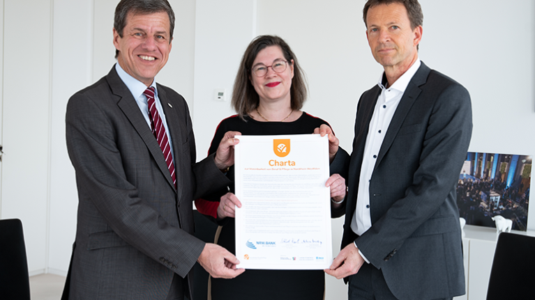 NRW.BANK-Vorstandsvorsitzender Eckhard Forst, Regine Jäger (Ansprechpartnerin für Beruf und Familie) und Achim Meierkamp, Bereichsleiter Personal, halten die unterzeichnete Charta für Beruf und Pflege.