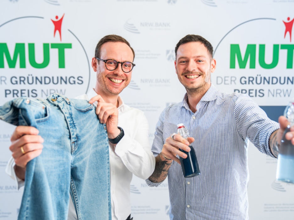 Felix Holtgrave und Dr. Maximilian Holtgrave von 140Fahrenheit vor dem MUT - DER GRÜNDUNGSPREIS NRW-Logo
