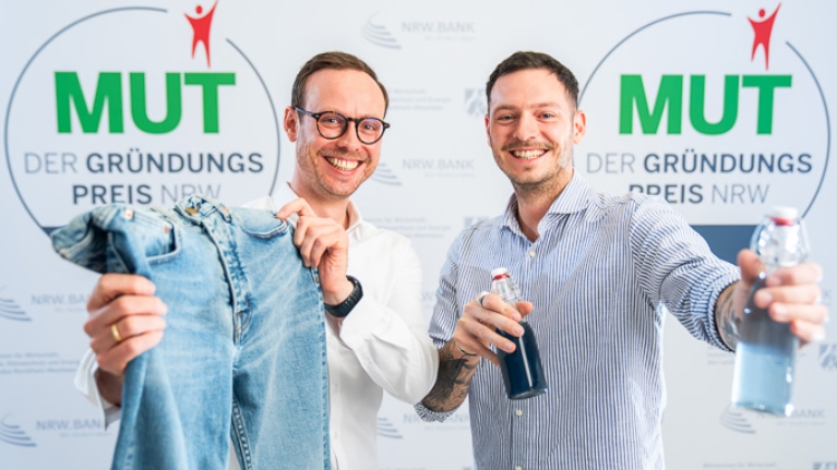 Felix Holtgrave und Dr. Maximilian Holtgrave von 140Fahrenheit vor dem MUT - DER GRÜNDUNGSPREIS NRW-Logo
