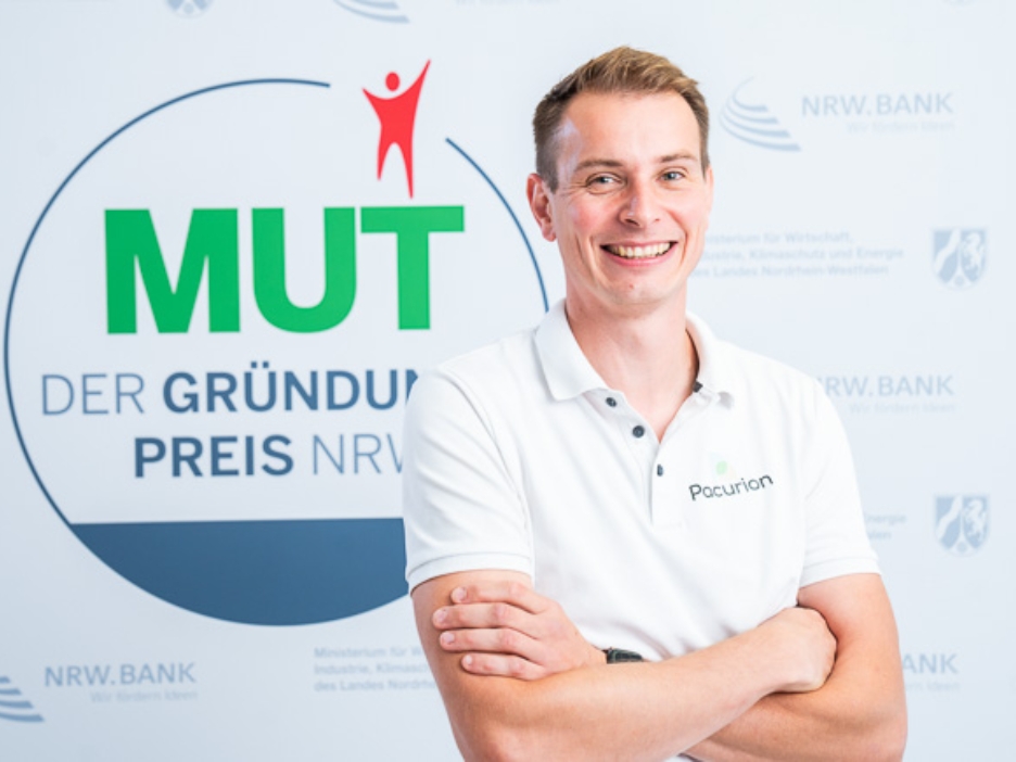 Dominik Leufgen von Pacurion vor dem MUT - DER GRÜNDUNGSPREIS NRW-Logo