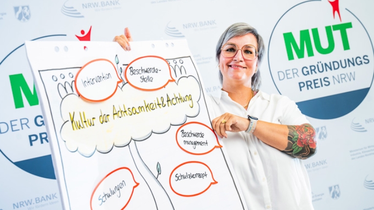 Vera Sadowski von Sicher(l)Ich vor dem MUT - DER GRÜNDUNGSPREIS NRW-Logo