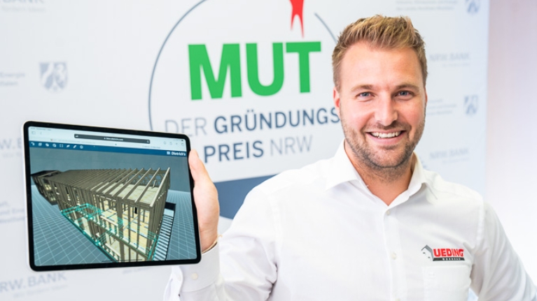 Manuel Ueding von Ueding Wohnbau vor dem MUT - DER GRÜNDUNGSPREIS NRW-Logo