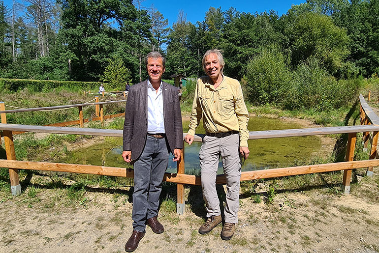 Eckhard Forst und Dr. Jan Boomers vor einem eingezäunten Teich, umgeben von Bäumen