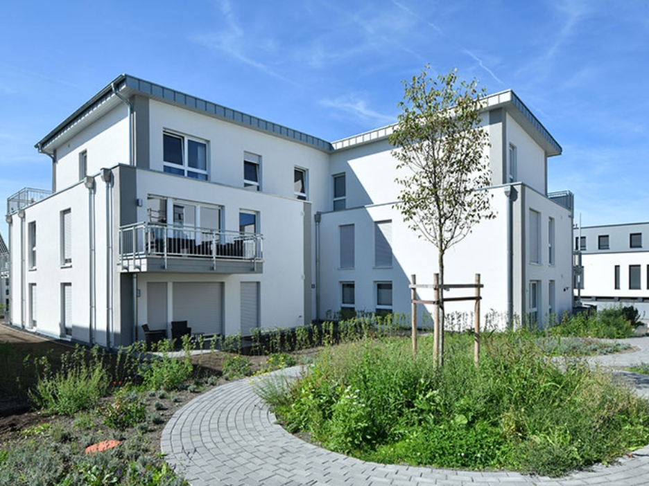 Modernes Wohnhaus mit Balkonen, gepflegter Grünfläche und geschwungenem Weg bei blauem Himmel.