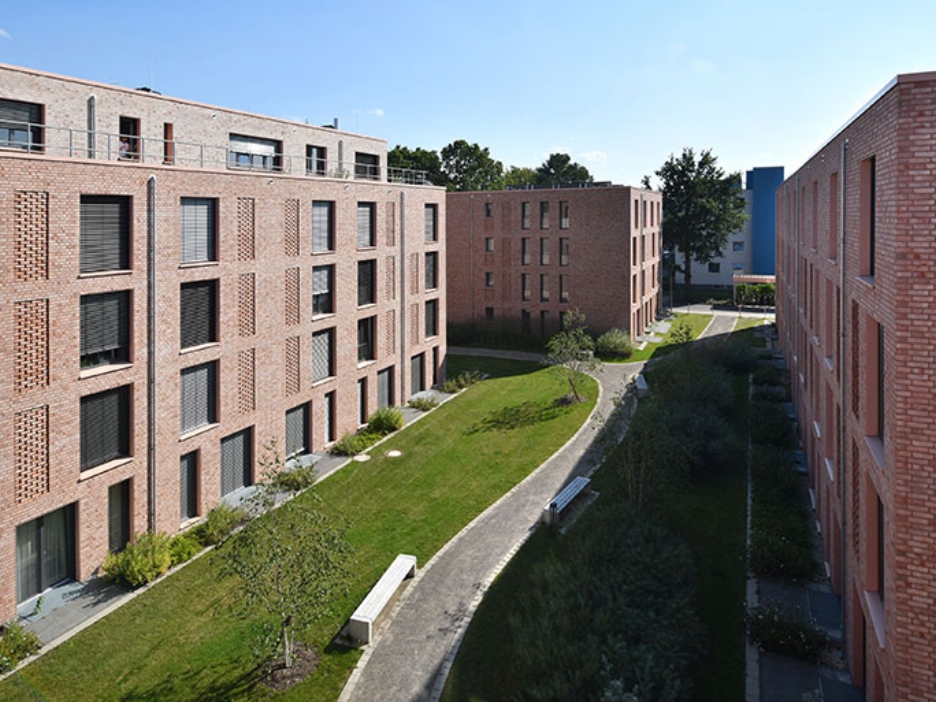 Zwischen mehreren Klinkergebäuden schlängelt sich ein grüner Weg durch die moderne Wohnanlage und schafft ruhige Rückzugsorte für Studierende.