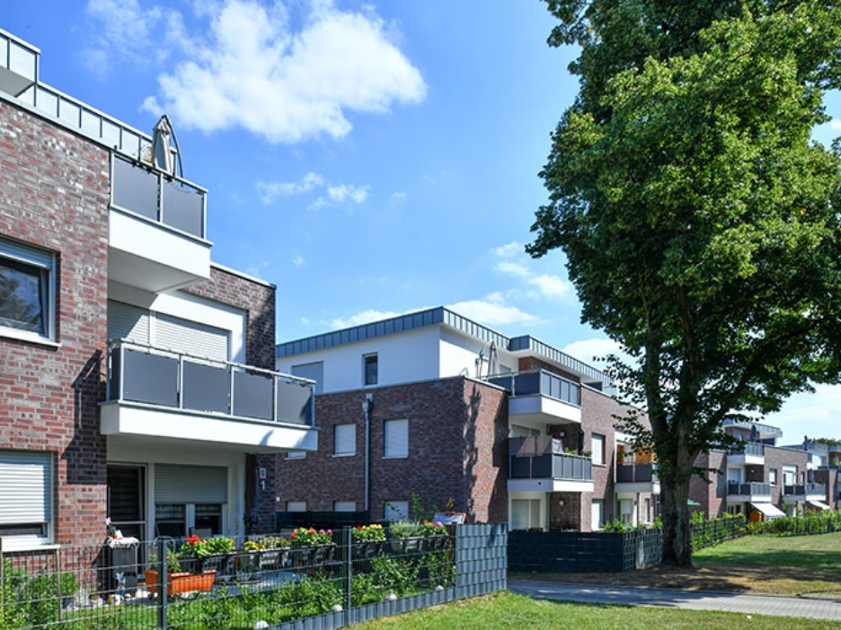 Backsteinanlage mit Balkonen, Gärten und großem Baum in einer sonnigen, ruhigen Nachbarschaft.