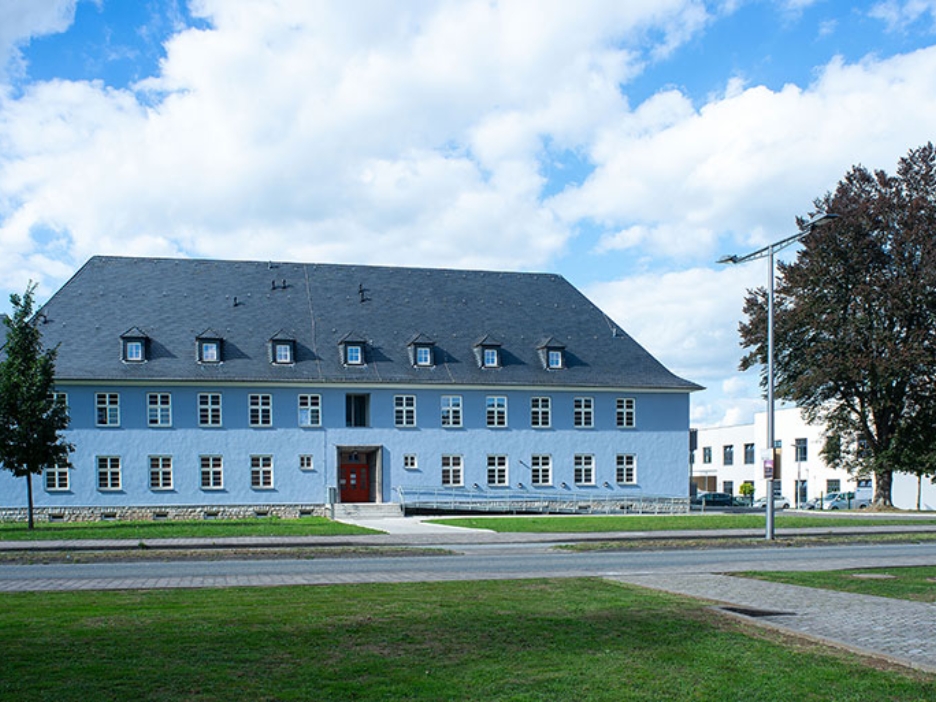 Historisches blaues Gebäude mit Schieferdach und vielen Fenstern vor einer grünen Anlage.