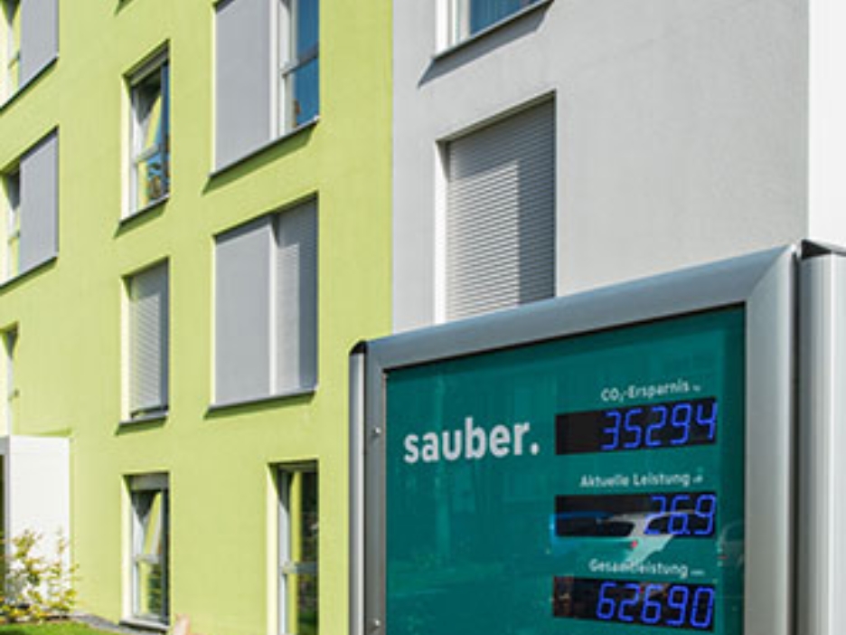Digitales Display vor grüner Fassade zeigt CO₂-Ersparnis und Leistung des Mieterstroms.