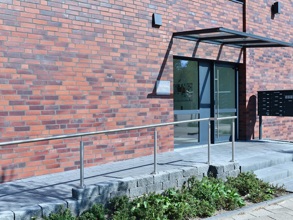 Moderner Eingang mit Backsteinfassade, Rampe und Glasvordach führt barrierefrei ins Gebäude.