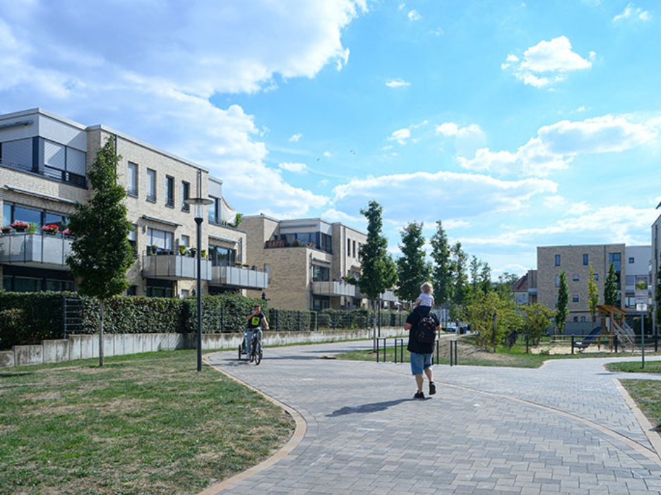 Wege durch eine gepflegte Wohnanlage mit Spielplatz, Grünflächen und Menschen an einem sonnigen Tag.