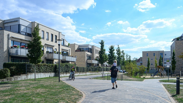 Wege durch eine gepflegte Wohnanlage mit Spielplatz, Grünflächen und Menschen an einem sonnigen Tag.