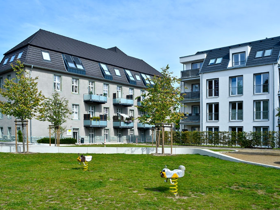 Spielplatz und Grünflächen vor sanierten Wohngebäuden mit Balkonen und hellem Fassadenbild.