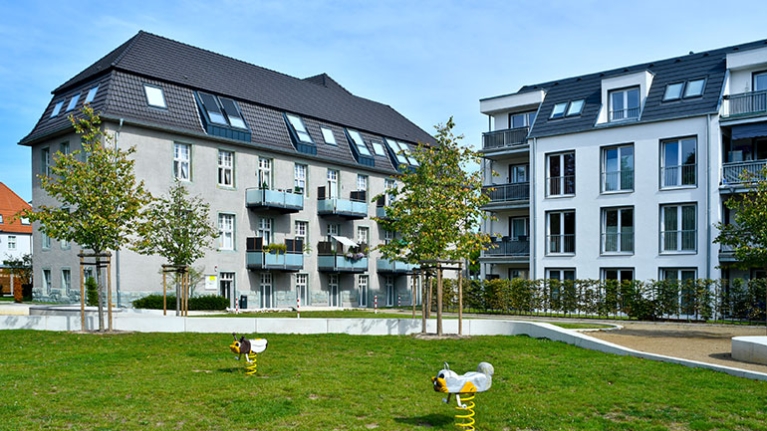 Spielplatz und Grünflächen vor sanierten Wohngebäuden mit Balkonen und hellem Fassadenbild.