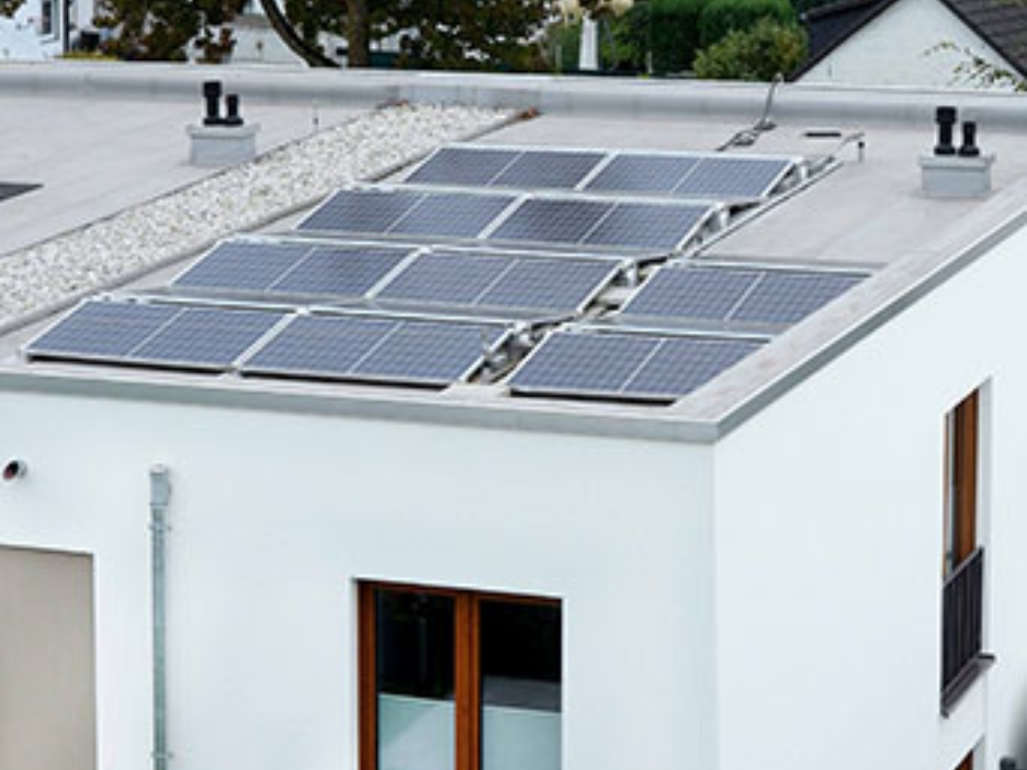 Solaranlage auf Flachdach eines Neubaus mit Blick auf umliegende Wohnhäuser und Herbstbäume.