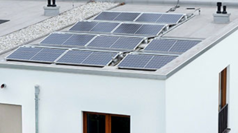 Solaranlage auf Flachdach eines Neubaus mit Blick auf umliegende Wohnhäuser und Herbstbäume.