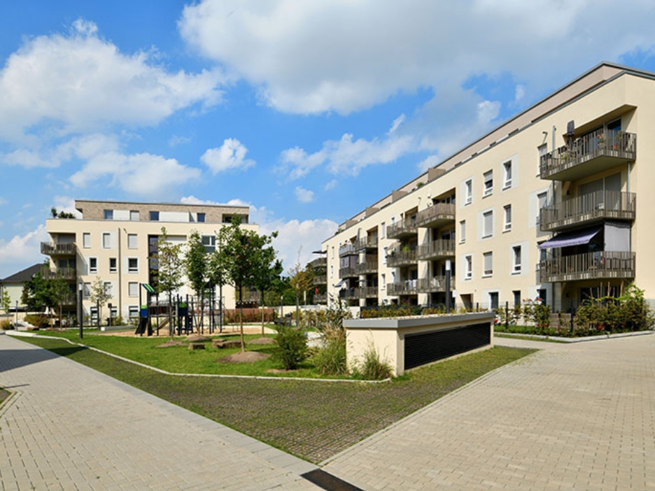 Helle Wohngebäude und ein grüner Innenhof bilden ein ruhiges Quartier, in dem Spielbereiche und Wege zum Verweilen einladen.