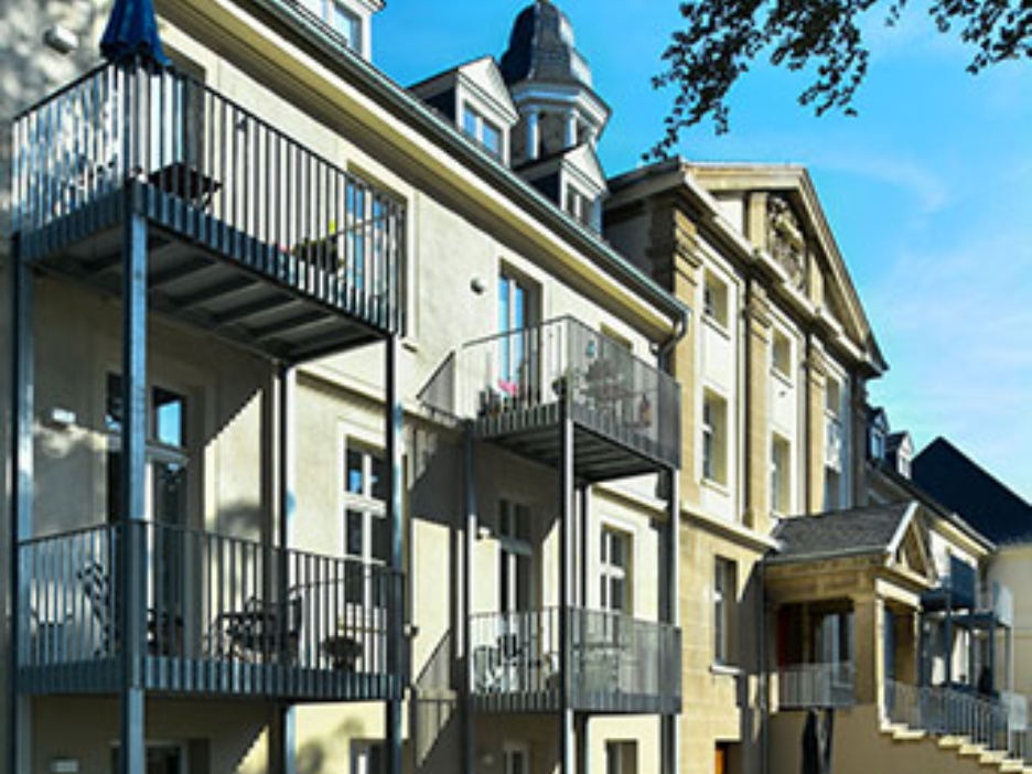 Seitlicher Blick auf das historische Gebäude mit Balkonen und hellem Mauerwerk im Sonnenlicht