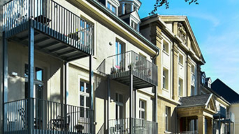 Seitlicher Blick auf das historische Gebäude mit Balkonen und hellem Mauerwerk im Sonnenlicht