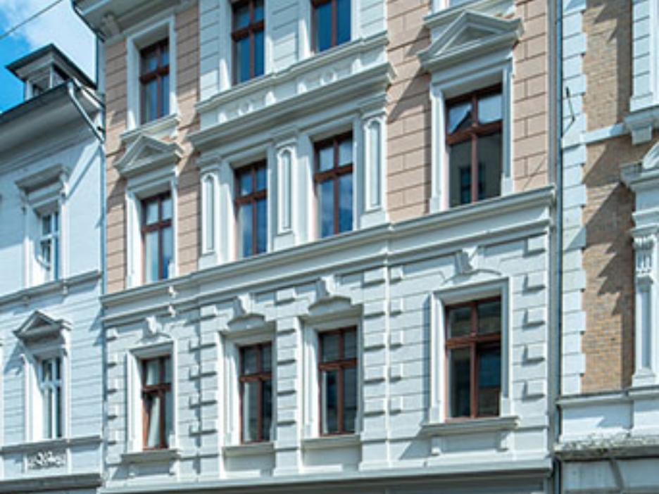 Sanierter Altbau mit detailreicher Fassade und dunklen Fenstern unter hellem Himmel.