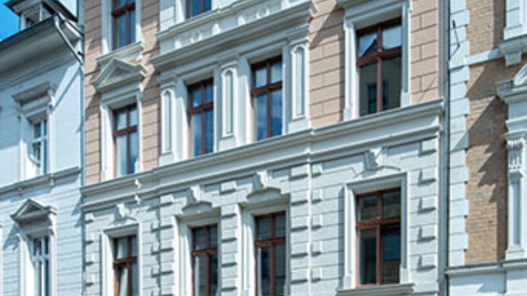 Sanierter Altbau mit detailreicher Fassade und dunklen Fenstern unter hellem Himmel.