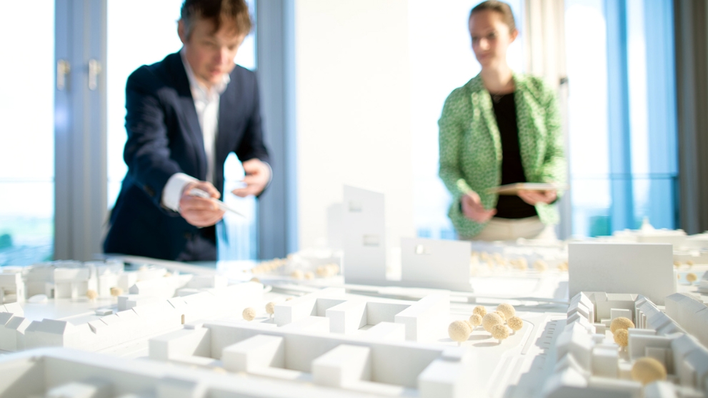 Ein Mann und eine Frau stehen vor dem Modell einer Stadt und diskutieren.