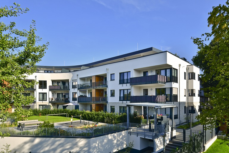 Ein kleiner Spielplatz und Grünflächen vor einem bogenförmigen Mehrfamilienhaus.