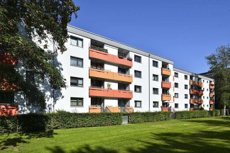 Eine großzügige Grünfläche erstreckt sich vor einem Reihen-Mehrfamilienhaus.