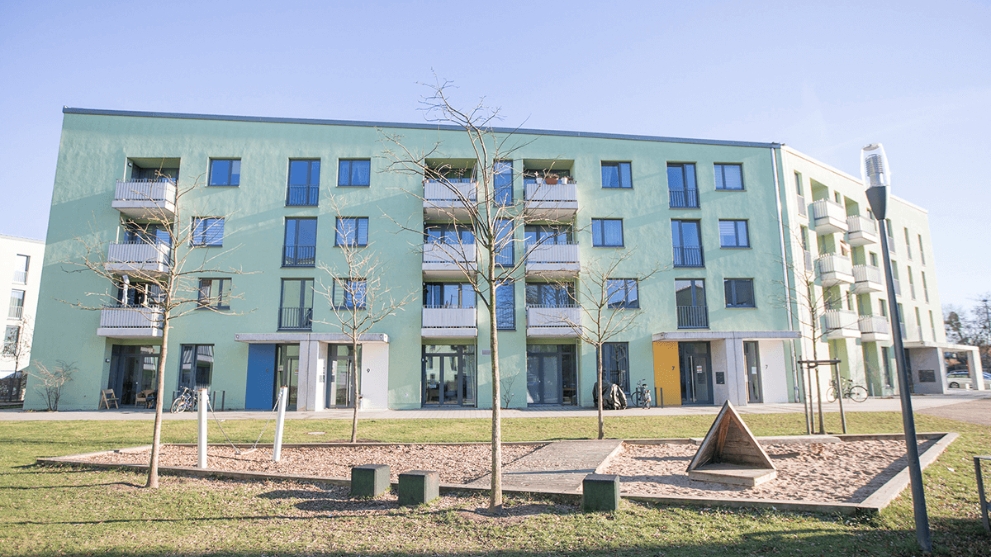 Mehrfamilienhaus mit hellgrüner Fassade, im Vordergrund ein Spielplatz