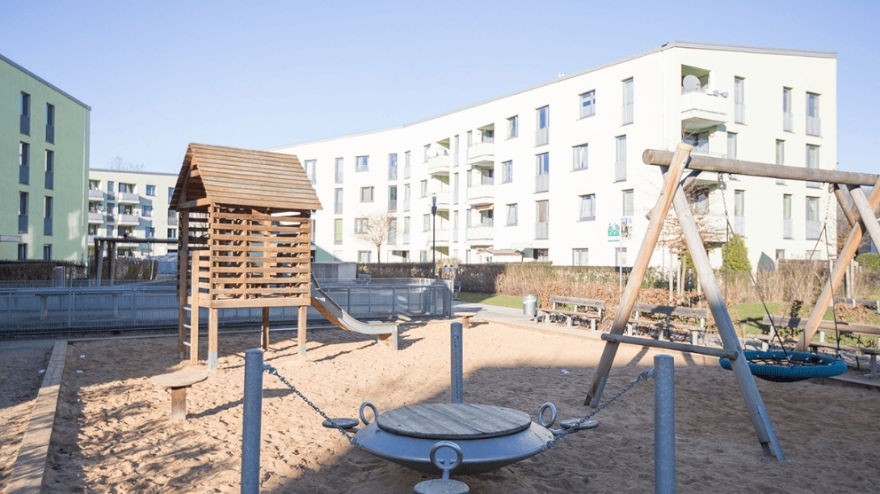Modernes Mehrfamilienhaus von außen mit einem Spielplatz im Vordergrund