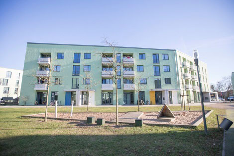 Mehrfamilienhaus mit hellgrüner Fassade, im Vordergrund ein Spielplatz