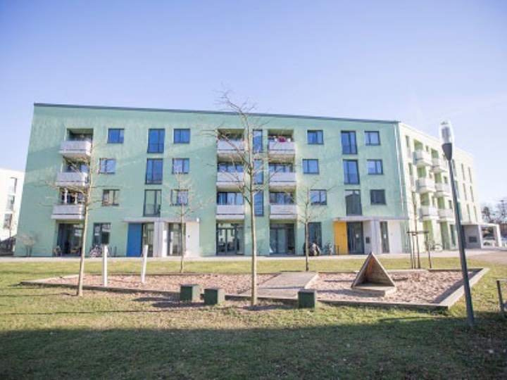 Mehrfamilienhaus mit hellgrüner Fassade, im Vordergrund ein Spielplatz