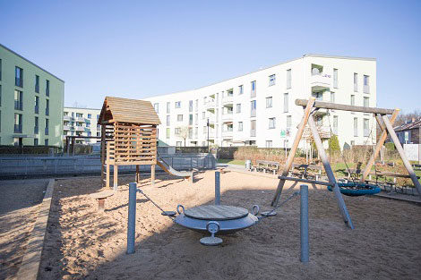 Modernes Mehrfamilienhaus von außen mit einem Spielplatz im Vordergrund