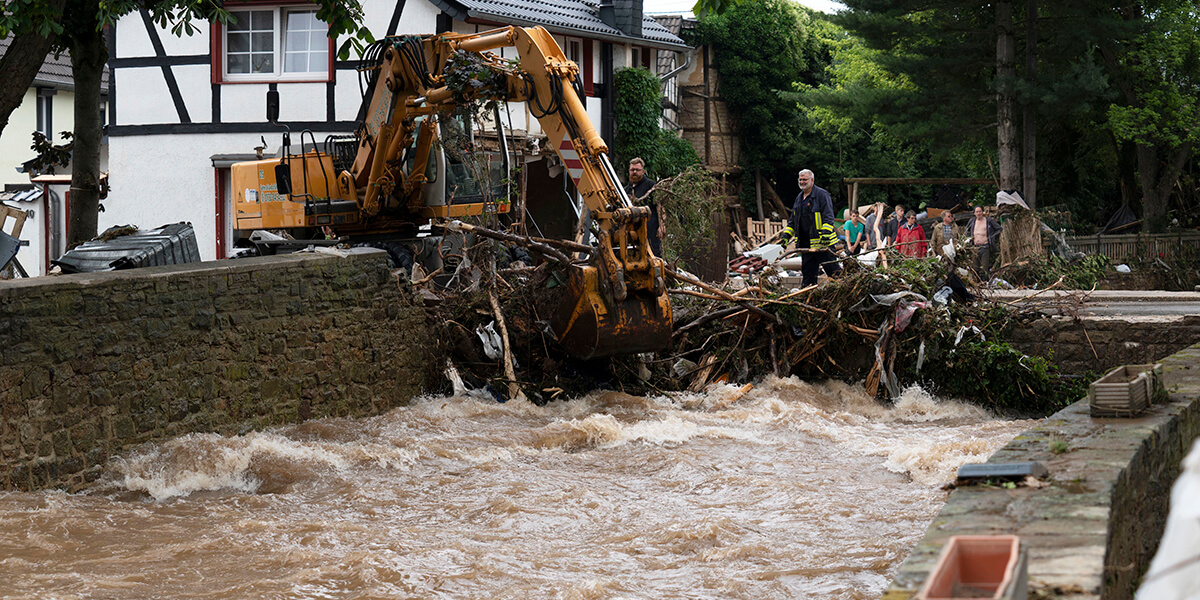Bagger bei Räumungsarbeiten vor einem Fachwerkhaus an einem Fluss nach den Unwettern in der Eifel.
